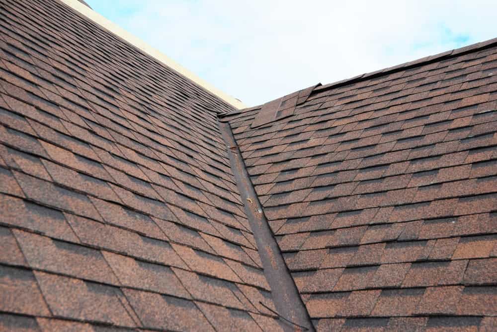 A close-up view of a residential roof with brown asphalt shingles. The image prominently shows the valley where two slopes of the roof meet, with clean and well-maintained shingles extending towards the sky, highlighting expert Siding Buchanan County services.